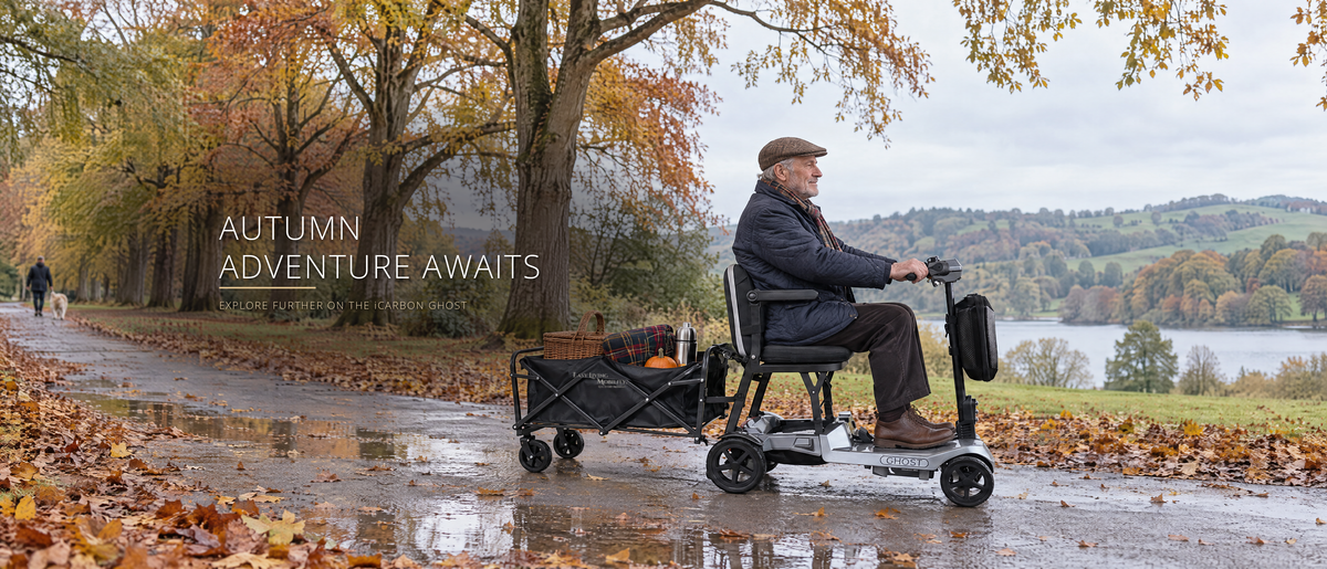 Autumn Adventure Awaits - older man riding an iCarbon Ghost folding mobility scooter towing a loaded trailer along an autumn woodland path