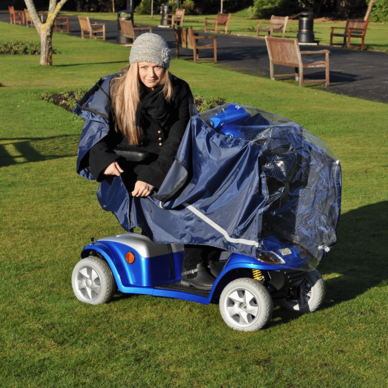 Person kneeling next to a blue mobility scooter with a cover on a grassy area.