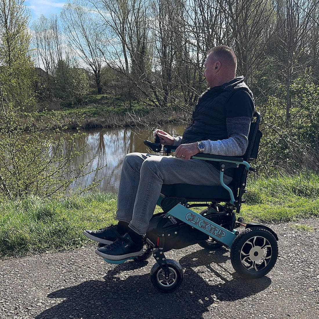 Man using a mobility scooter by a pond with trees in the background