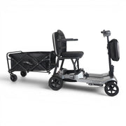 A mobility scooter with a rear cargo wagon attachment, shown on a clean white studio background. The scooter is primarily gray and black, with the black seat, wheels, and wagon bed clearly visible.