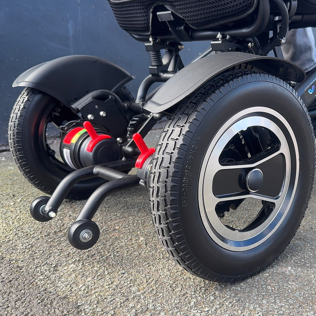 Close-up of a power wheelchair with visible wheels on a pavement.