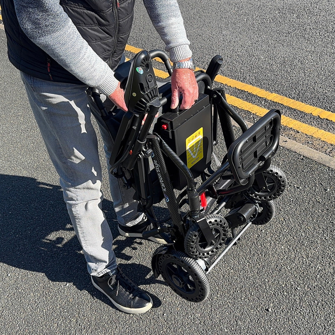 Person holding a folded electric scooter on a road with yellow lines.