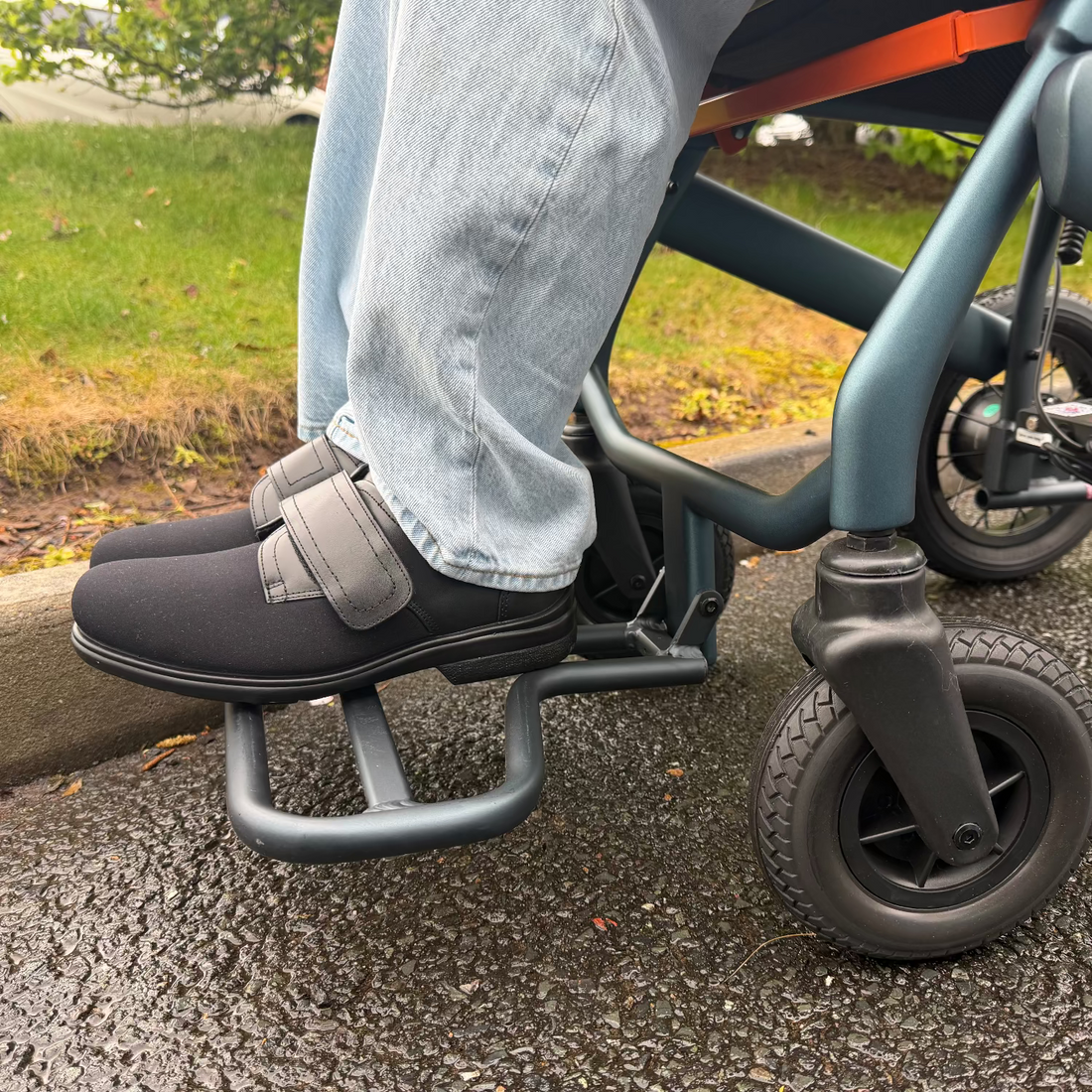 Person using electric wheelchair on a sidewalk with grass and a car in the background