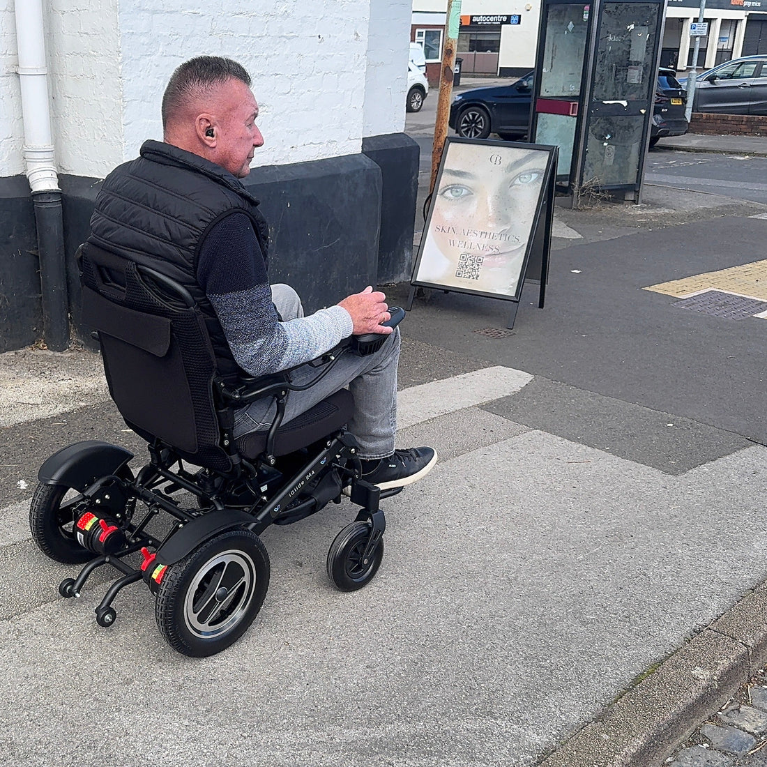 Man in a power wheelchair on a sidewalk with a building and street in the background